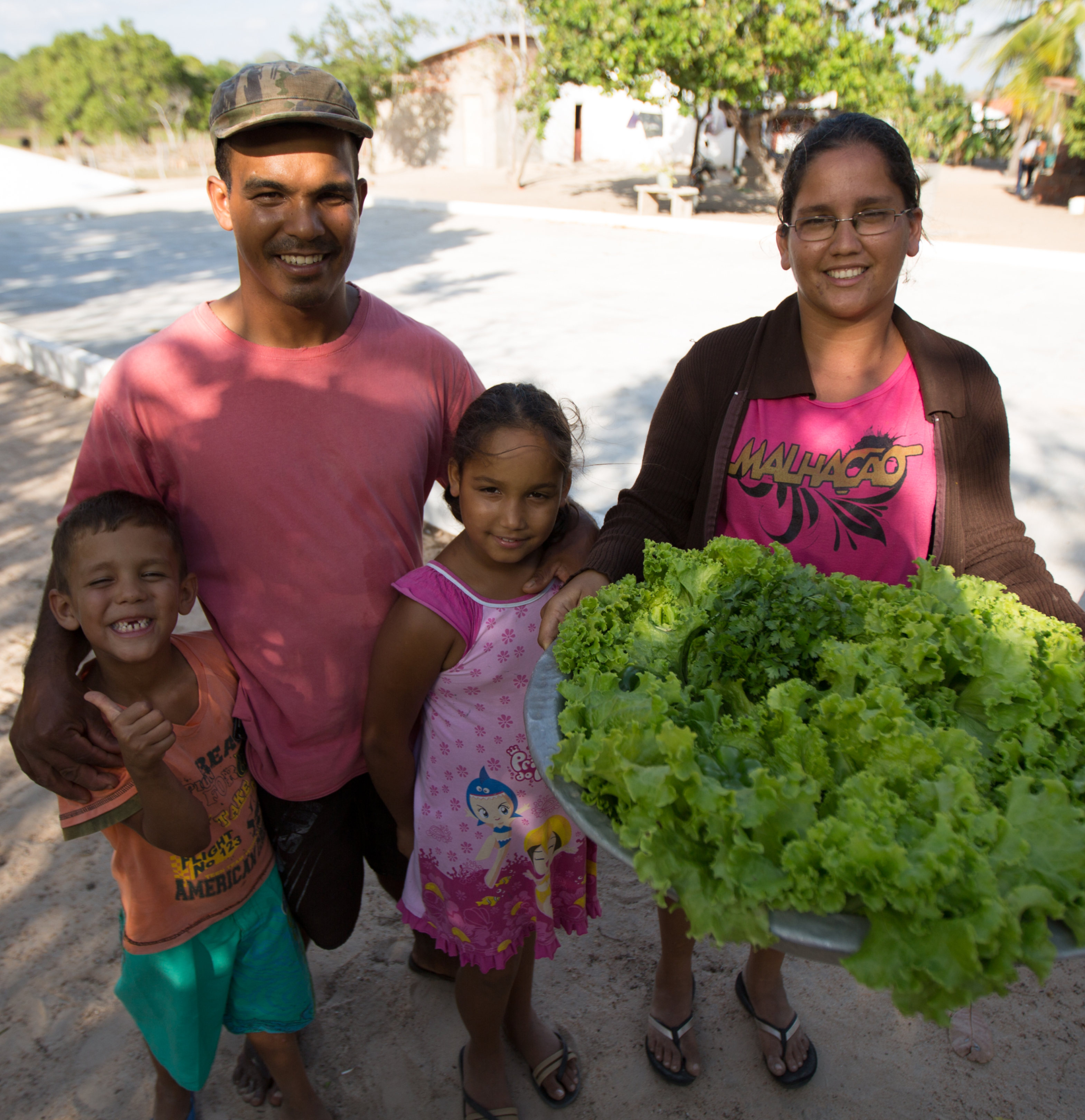 Família em frente a cisterna, com uma bacia de verduras